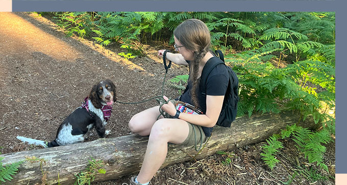 a lady training a puppy on a lead while sitting on a fallen tree log